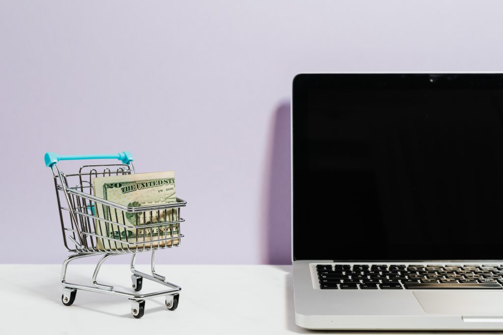 Imagem com computador ao lado de uma nota em dólar, representando a compra on-line